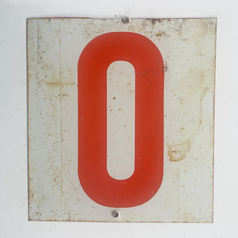 May include: Vintage metal sign featuring a bold red number zero on a white background. The sign has a rectangular shape with visible signs of wear and tear, including rust and discoloration, adding to its antique charm. Two rivets secure the sign.