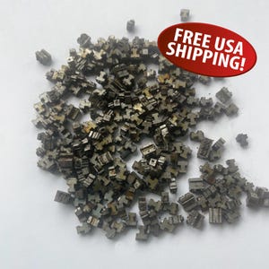 May include: A pile of small, metallic, T-shaped components scattered on a white surface. The components appear to be made of a dull, silver-colored metal. The image includes a red oval with the text "FREE USA SHIPPING!"
