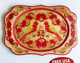 May include: A decorative wooden serving tray with a gold background and a red scalloped border. The tray features a vibrant folk art design of two red birds, flowers, and foliage in red, orange, and green. The tray is oval-shaped.