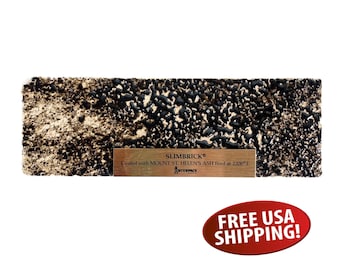 May include: A rectangular Slimbrick sample with a textured surface, featuring a mix of black and tan tones. The brick has a small wooden label with the text "SLIMBRICK®" and details about the ash used. The brick is coated with Mount St. Helen's ash.