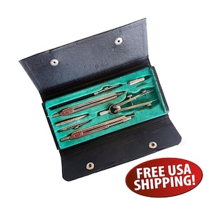 May include: A black leather-like folding case containing a set of silver-toned metal drafting compasses and technical drawing tools. The interior of the case is lined with bright green fabric, featuring molded slots to hold each tool securely.