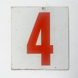 May include: A rectangular white metal sign featuring a large, bold red number 4. The sign has a slightly weathered appearance with some rust around the edges and a small hole at the top for hanging.