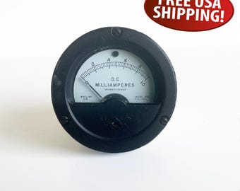 May include: A black, circular D.C. milliammeter with a white face and a needle indicator. The face displays the text "D.C. MILLIAMPERES" and numerical markings from 0 to 10. The meter is marked "WACLINE 21" and "MODEL AS F.S.TINA".