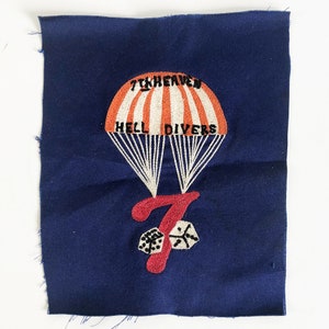 May include: A blue fabric patch with an embroidered image of a parachute with the text "7th Heaven Hell Divers" and a large number "7" with two dice below it.