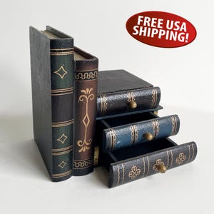 May include: A decorative storage chest designed to resemble a stack of three vintage books. The exterior features dark green, brown, and black finishes with gold-colored filigree patterns and small round knobs on each of the three pull-out drawers.