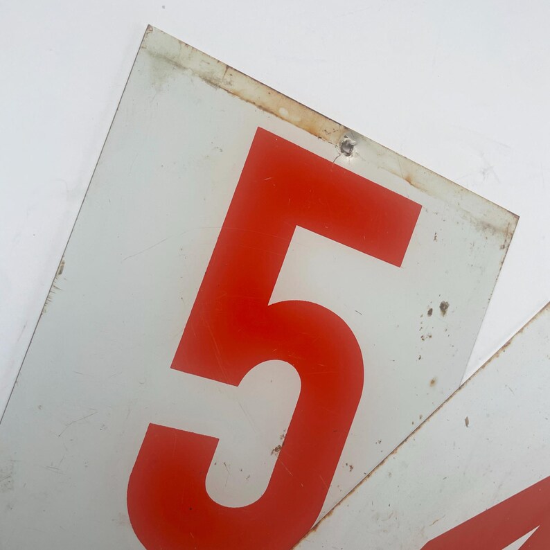 May include: Two rectangular white metal signs with the number 5 in red. The signs have a distressed appearance with some rust and wear. The signs are likely vintage or industrial.