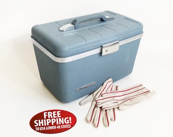 May include: A vintage blue hard-sided travel case with a silver latch and handle. The case has a silver trim around the edges. The case is sitting on a white surface with a pair of white gloves with red stripes.