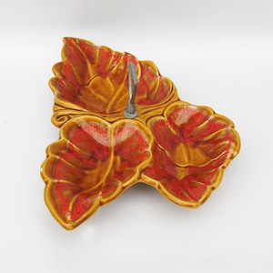 May include: A three-sectioned ceramic serving dish with a metal handle. The dish is shaped like leaves and is decorated with a brown and orange glaze.