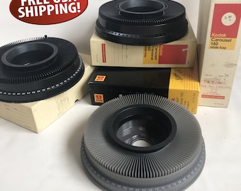 May include: Three black and gray slide carousels with a black center and a numbered ring around the edge. The carousels are on top of boxes that say "Kodak Carousel 140 slide tray" and "Tetons for all Sensens".