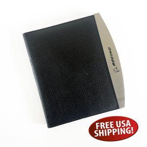 May include: Black leather-bound notebook with a silver accent. The silver accent features the word "BOEING" and a logo. The notebook has a textured surface and appears to be new.
