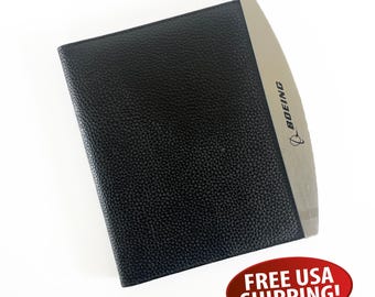 May include: Black leather-bound notebook with a silver accent. The silver accent features the word "BOEING" and a logo. The notebook has a textured surface and appears to be new.
