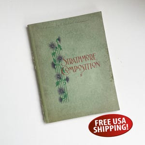 May include: A vintage Strathmore Composition book with a faded green cover. The cover features a floral design with purple flowers and green stems, and the title is in red script. The book is slightly worn, suggesting age.
