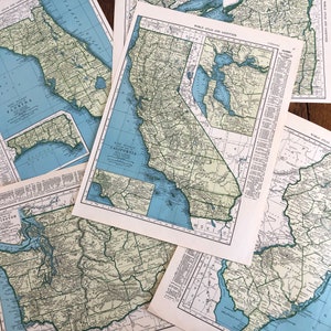 May include: A collection of vintage maps of California, Washington, and Florida. The maps are printed on paper and have a light blue and green color scheme. The maps are titled "Rand McNally of California", "World Atlas and Gazetteer", and "World Atlas".