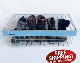 May include: A wire basket with a light blue front panel displaying the text "Outdoor Storage" and a logo. The basket contains five pairs of boots in various shades of brown and black. The boots are arranged inside the basket.