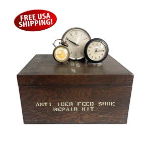 May include: A wooden box with the text "ANTI ICER FEED SHOE REPAIR KIT" printed on the front. Three clocks are sitting on top of the box, including a small alarm clock with a yellow face.