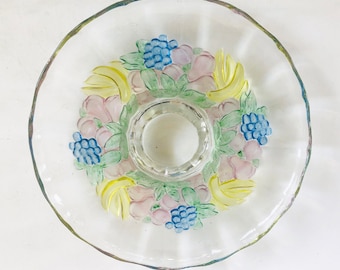 May include: A clear glass fruit bowl with a raised design of pink, yellow, and blue fruit. The bowl has a center pedestal.