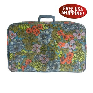 May include: Vintage floral suitcase with a blue handle and trim. The suitcase features a colorful pattern of large flowers in shades of blue, orange, and purple on a green background. The suitcase is rectangular and appears to be made of a durable material.