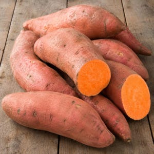 May include: A collection of raw sweet potatoes with copper-colored skin and bright orange flesh. Several of the sweet potatoes are whole and elongated, while two are sliced crosswise to reveal the vibrant, solid orange interior texture.