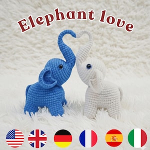 Könnte beinhalten: Zwei gehäkelte Elefantenfiguren, einer blau und einer weiß, deren Rüssel ein Herz bilden. Der Text "Elephant love" steht über den Elefanten. Die Figuren stehen auf einer weißen, flauschigen Oberfläche.