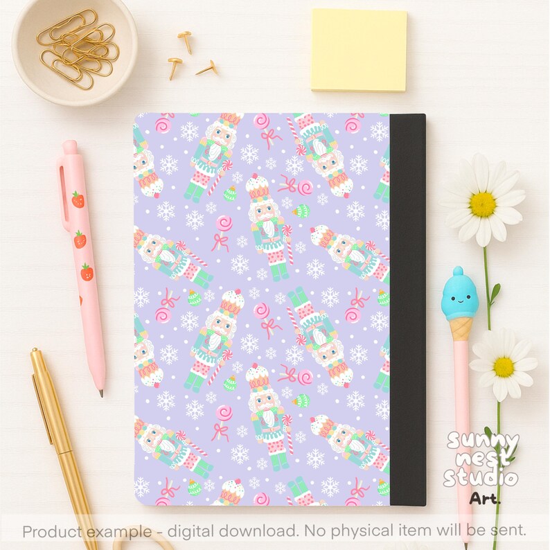 Pu&ograve; includere: Un taccuino con una copertina lavanda con un motivo ripetuto di schiaccianoci, fiocchi di neve e caramelle. Il taccuino ha un dorso nero. L'immagine include penne, graffette e fiori. Il testo sull'immagine recita "Sunny Nest Studio Art."