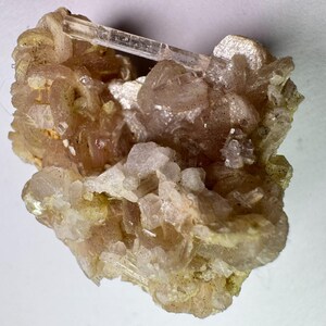 May include: A close-up of a mineral specimen featuring a cluster of light brown and clear crystals. The crystals have a rough, textured appearance, with some areas appearing more translucent than others. The overall color palette is a mix of beige, tan, and clear.