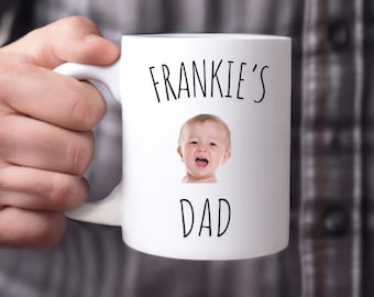 Op de afbeelding: Witte keramische mok met een zwart-witte afbeelding van een baby en de tekst "Frankie's Dad".