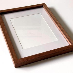 May include: A rectangular wooden picture frame with a white mat. The frame is made of dark brown wood and has a simple, modern design. The mat opening is a rectangle, ready for a photo or artwork.