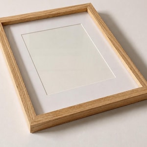 May include: A rectangular picture frame constructed from light-colored natural wood with a visible grain pattern. The frame features a clean, white mat board insert surrounding a central rectangular opening, providing a neutral display area.