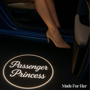 May include: A car door with a projected light on the ground that reads "Passenger Princess" in a white, elegant font. The image also shows a person wearing beige high heels and the text "Made For Her".