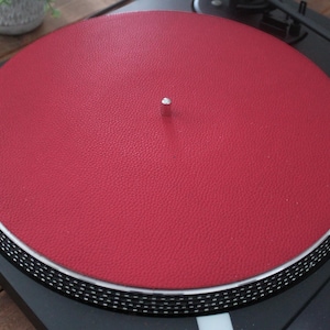 May include: A red leather turntable slipmat with a textured surface. The slipmat is designed to fit a standard 12-inch turntable.