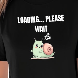 May include: Black t-shirt featuring a cartoon snail with a pink shell and a confused expression. The text "LOADING... PLEASE WAIT" is printed above the snail in white. The snail is light green.