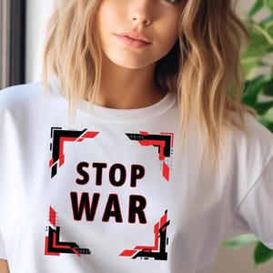Può includere: T-shirt bianca con la scritta "STOP WAR" in lettere rosse, incorniciata da un design geometrico nero e rosso. La maglietta è in stile casual, adatta all'uso quotidiano.