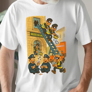 May include: White t-shirt with a cartoon illustration depicting a robbery. The design shows burglars on a ladder, breaking into a building marked "Musee du Loup", with police playing cards below. The image is colourful and humorous.