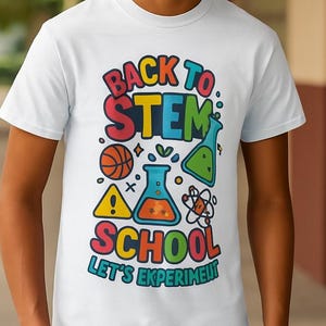 Può includere: T-shirt bianca con una grafica colorata che dice "BACK TO STEM SCHOOL" con illustrazioni a tema scientifico. Il design include un pallone da basket, un becher e un simbolo di atomo. La maglietta ha anche il testo "LET'S EXPERIMENT!"