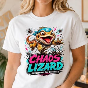 Può includere: T-shirt bianca con grafica colorata di una lucertola e la scritta "Chaos Lizard Professional Bug Destroyer". Il design include una lucertola, insetti e colori vivaci. La maglietta è un capo casual.