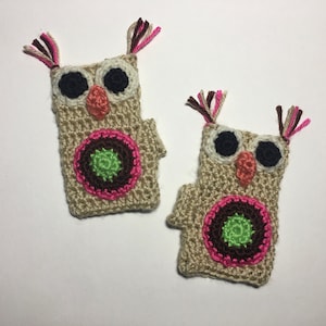 May include: Two crocheted owl ornaments with brown, pink, and green details. The owls have large black eyes and a pink beak.