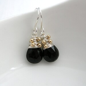 May include: A pair of silver dangle earrings with black gemstone drops. The earrings are accented with gold beads.