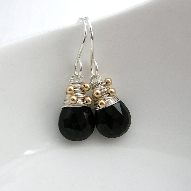 May include: A pair of silver dangle earrings with black gemstone drops. The earrings are accented with gold beads.