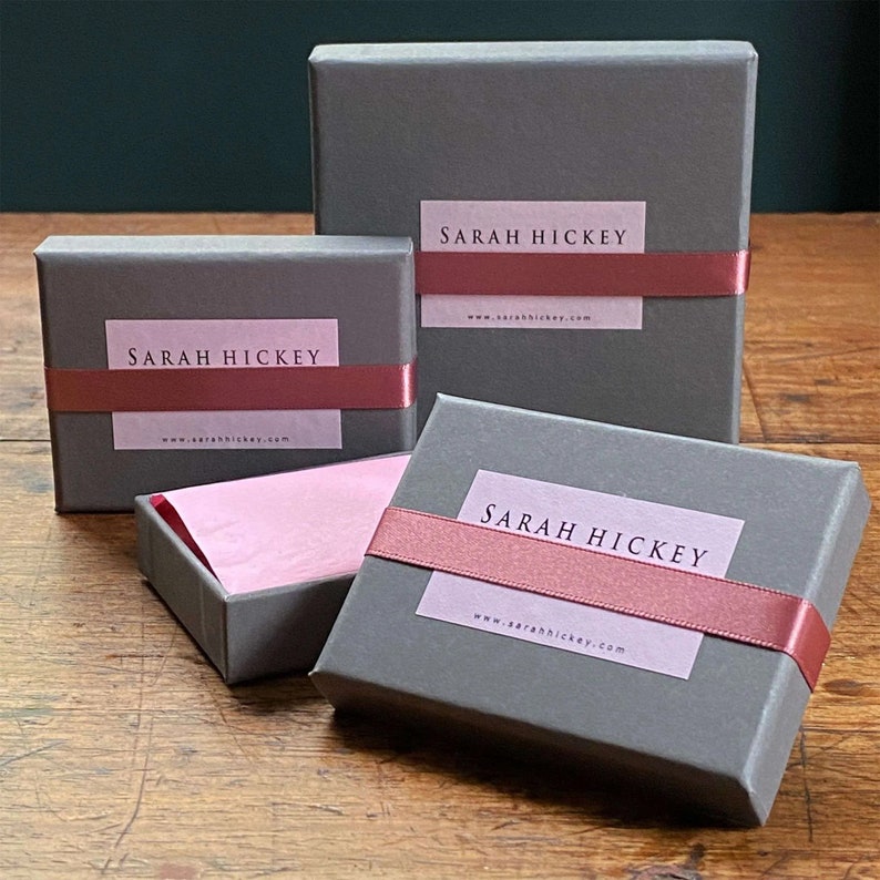 May include: Three gray gift boxes with pink ribbon and a white label that says "SARAH HICKEY" and "www.sarahhickey.com".
