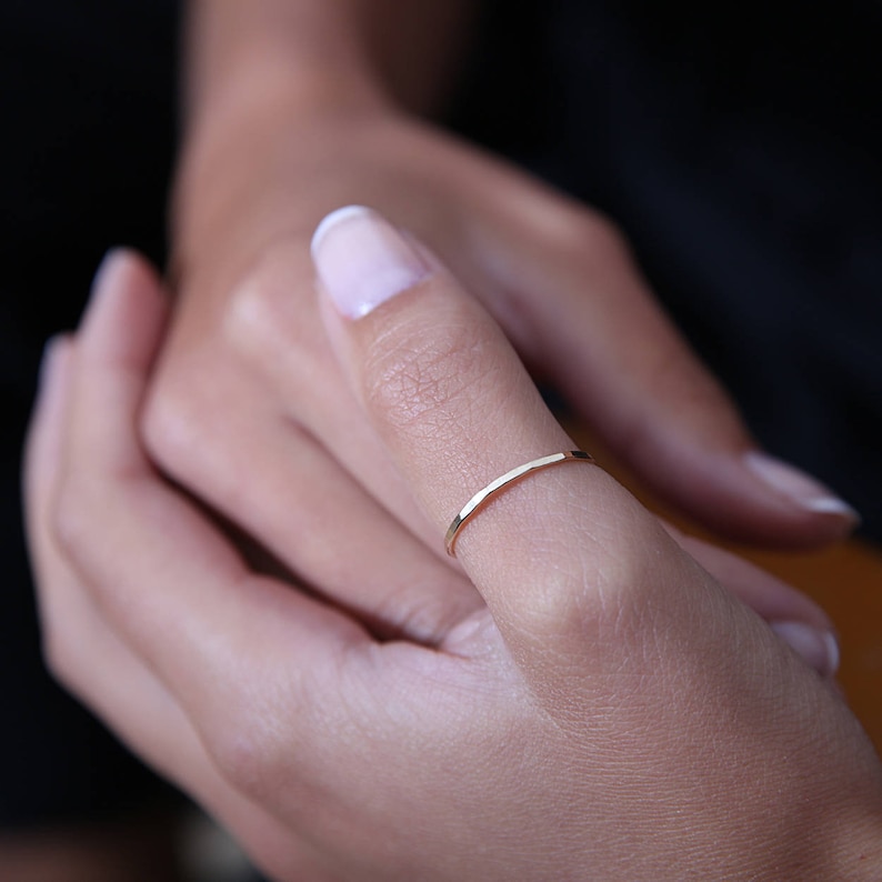 May include: A thin gold band ring worn on a person's thumb.
