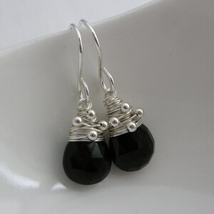 May include: A pair of silver dangle earrings with black gemstone drops. The earrings are made with silver wire wrapped around small silver beads and feature faceted black gemstones.