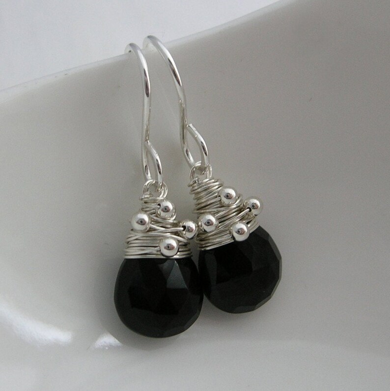 May include: A pair of silver dangle earrings with black gemstone drops. The earrings are made with silver wire wrapped around small silver beads and feature faceted black gemstones.