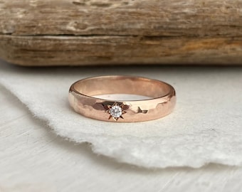 May include: A hammered rose gold band with a small, clear diamond set in a star shape.
