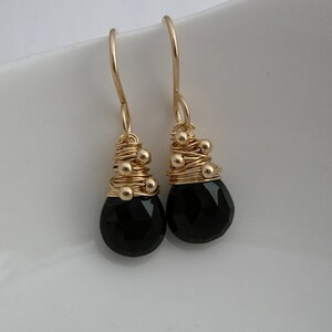 May include: A pair of gold earrings with black gemstone drops. The earrings feature a gold wire design with small gold beads.