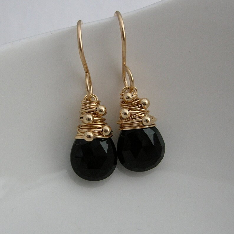 May include: A pair of gold earrings with black gemstone drops. The earrings feature a gold wire design with small gold beads.