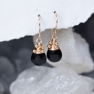 May include: A pair of gold earrings with black gemstone drops. The earrings are made with gold wire and have small gold beads around the top of the gemstone.