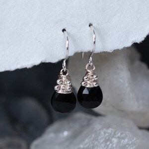 May include: Black onyx gemstone earrings with silver wire wrapped around the top and silver beads. The earrings are teardrop shaped.