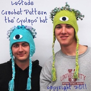 May include: Two people wearing crocheted hats with a single eye and long braids. The hats are green and blue. The text "Lastade Crochet Pattern the "Cyclops" hat" and "copyright 2011" are visible in the image.