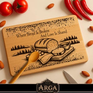 Könnte beinhalten: Rechteckiges Holzschneidebrett mit dem Text "Where Bread Is Broken And Love Is Shared" und einer Brotillustration. Ein Holzlöffel, Tomaten, Mandeln und rote Paprika umgeben das Brett.
