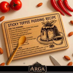 May include: A wooden recipe board for sticky toffee pudding, featuring etched text with ingredients and instructions. A wooden spoon lies on the board. The scene includes tomatoes, almonds, and red chilies. The board measures approximately 30 cm.